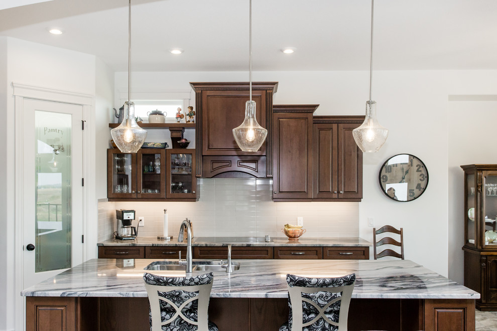 This is an example of a large transitional l-shaped eat-in kitchen in Calgary with raised-panel cabinets, brown cabinets, granite benchtops, white splashback, ceramic splashback, stainless steel appliances, ceramic floors, with island, a double-bowl sink, grey floor and grey benchtop.
