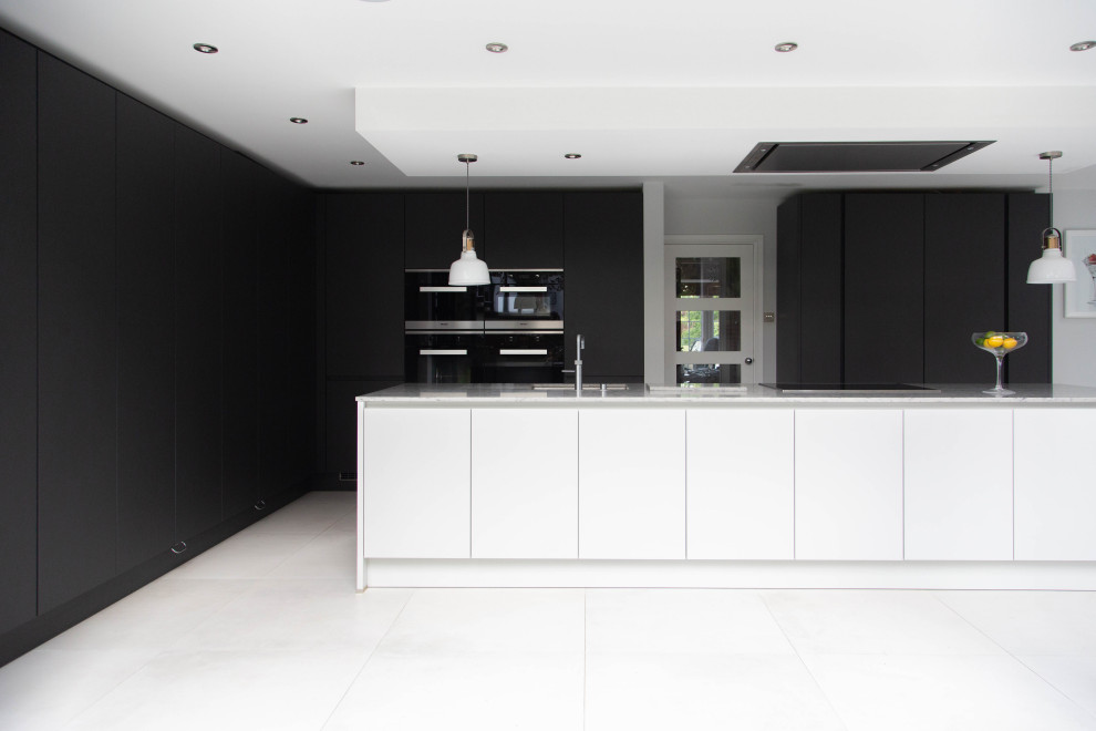 This is an example of a large contemporary galley open plan kitchen in London with flat-panel cabinets, with island, an undermount sink, black cabinets, panelled appliances, white floor and white benchtop.
