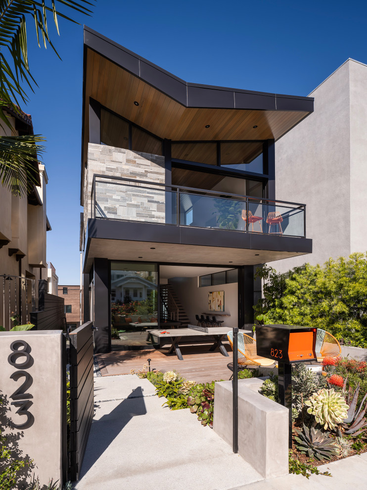Example of a large mid-century modern gray three-story stone house exterior design in Los Angeles with a butterfly roof, a metal roof and a black roof