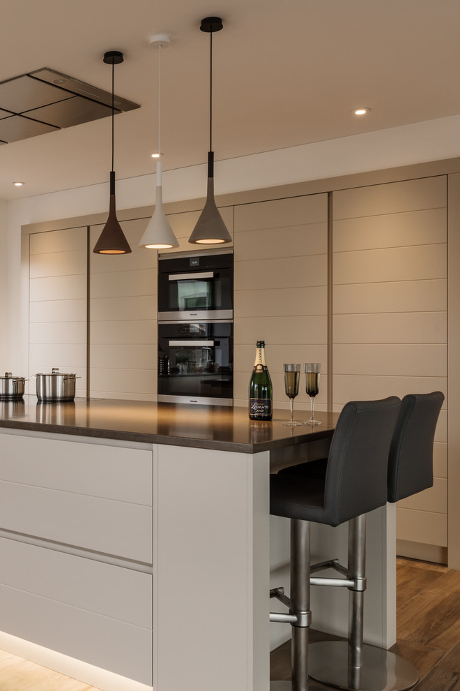 This is an example of a large contemporary open plan kitchen in Devon with beaded inset cabinets, grey cabinets, quartzite benchtops, black appliances and with island.
