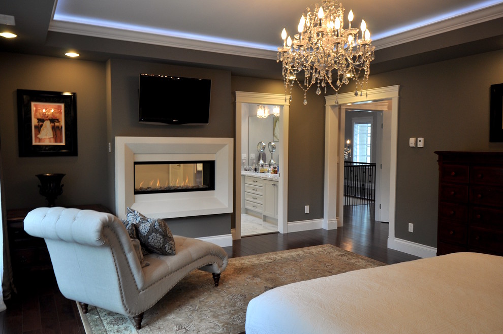 Inspiration for a large master bedroom with grey walls, dark hardwood floors, a two-sided fireplace, a plaster fireplace surround and brown floor.