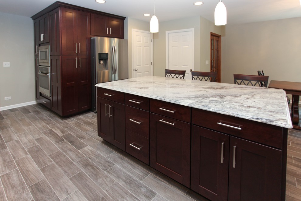 Example of a large transitional u-shaped porcelain tile eat-in kitchen design in Chicago with an undermount sink, recessed-panel cabinets, dark wood cabinets, granite countertops, gray backsplash, glass tile backsplash, stainless steel appliances and an island