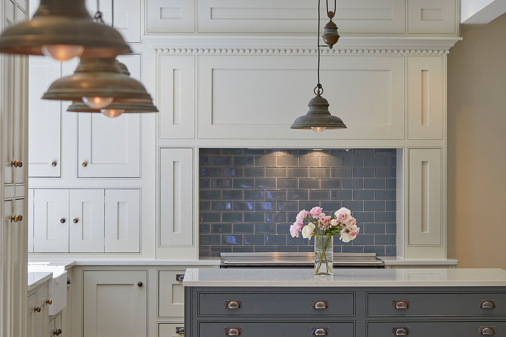 Design ideas for a large victorian l-shaped kitchen/diner in Surrey with a belfast sink, shaker cabinets, beige cabinets, composite countertops, grey splashback, porcelain splashback, black appliances, porcelain flooring, an island, beige floors and white worktops.