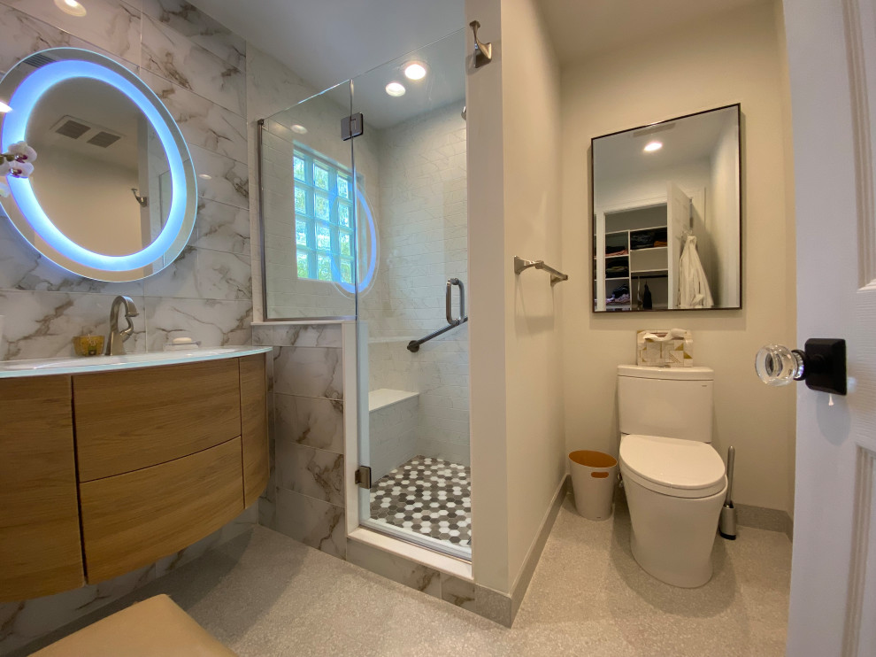 Пример оригинального дизайна: маленькая главная ванная комната в стиле модернизм с фасадами островного типа, светлыми деревянными фасадами, душем в нише, раздельным унитазом, бежевой плиткой, керамогранитной плиткой, белыми стенами, полом из керамогранита, монолитной раковиной, стеклянной столешницей, бежевым полом, душем с распашными дверями, белой столешницей, сиденьем для душа, тумбой под одну раковину и подвесной тумбой для на участке и в саду