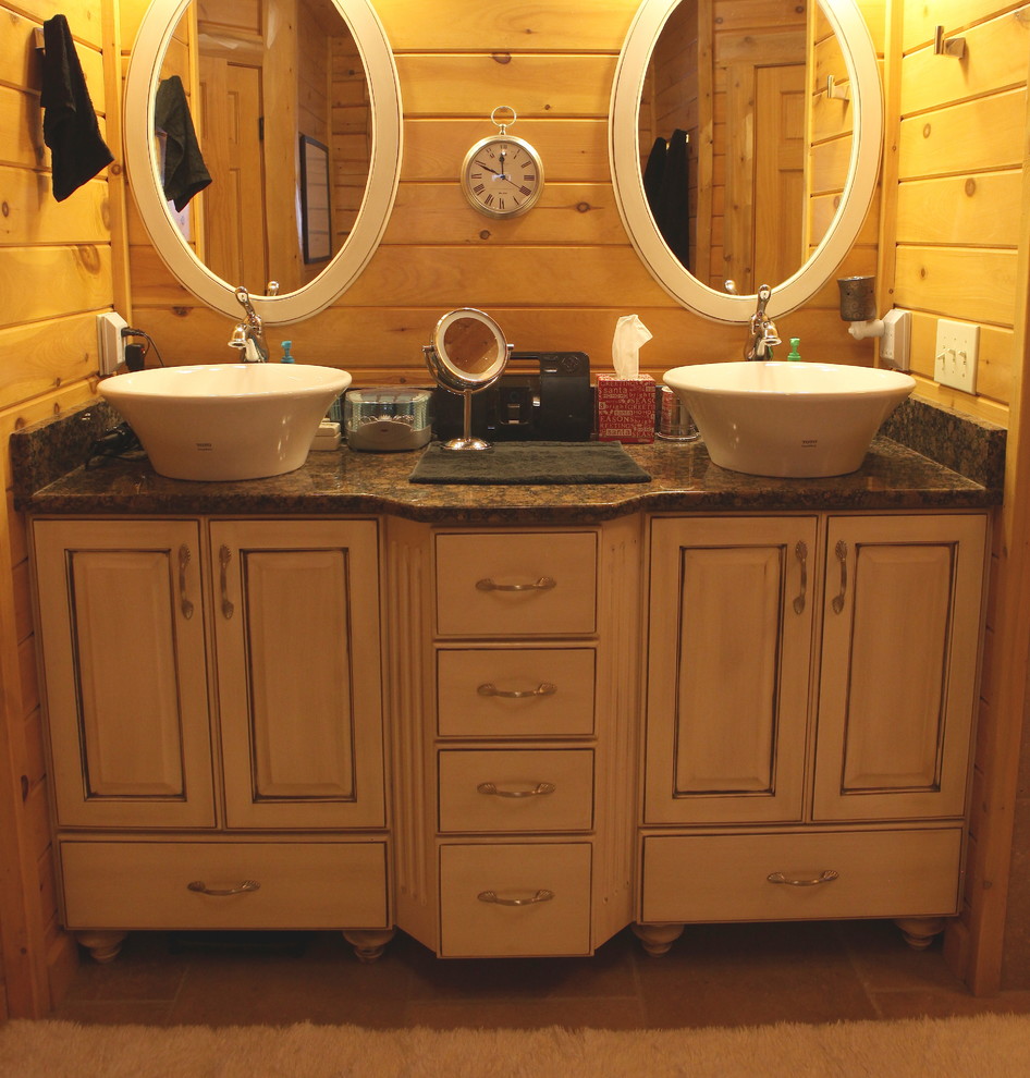 Example of a large mountain style master travertine floor and beige floor bathroom design with raised-panel cabinets, distressed cabinets, a vessel sink and granite countertops
