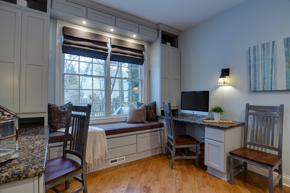 This is an example of a mid-sized arts and crafts study room in Chicago with blue walls, light hardwood floors, no fireplace, a built-in desk and brown floor.