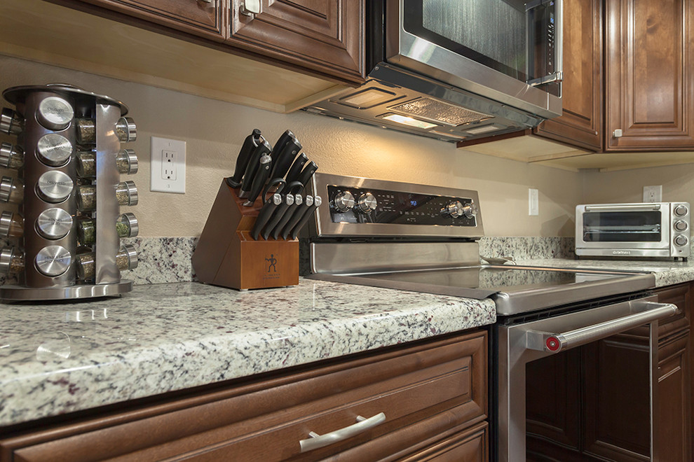 Example of a mid-sized transitional l-shaped laminate floor and brown floor enclosed kitchen design in Phoenix with an undermount sink, shaker cabinets, medium tone wood cabinets, granite countertops, multicolored backsplash, stone slab backsplash, stainless steel appliances and an island