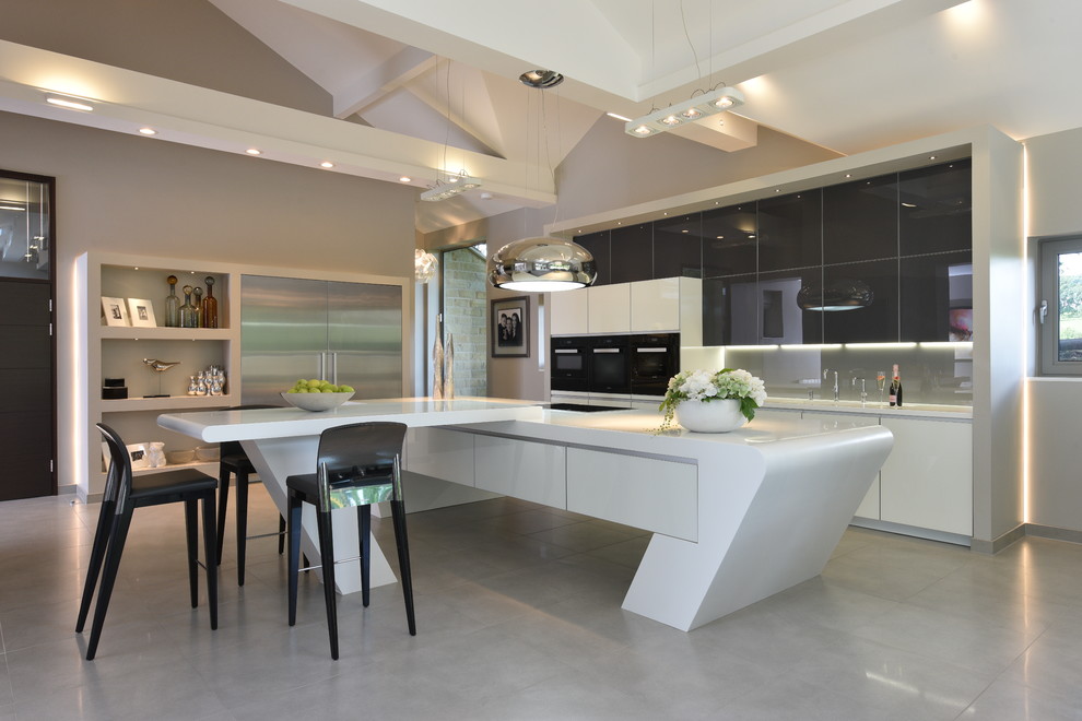 Design ideas for an expansive contemporary kitchen in Manchester with grey cabinets, solid surface benchtops, grey splashback, glass sheet splashback, black appliances, flat-panel cabinets, multiple islands and grey floor.