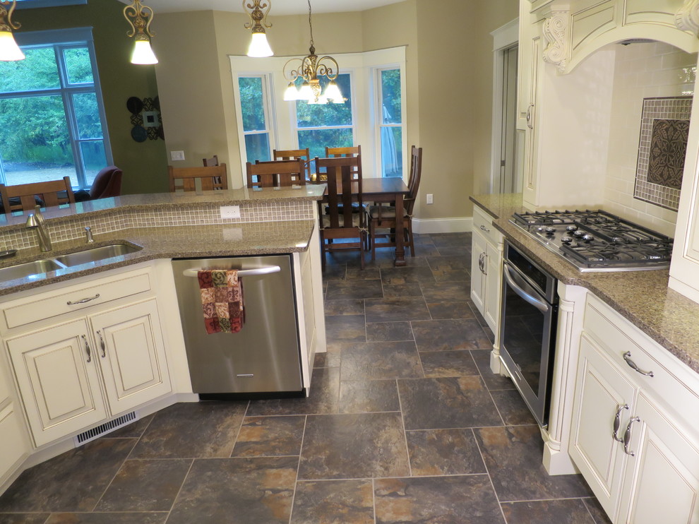 Example of a large transitional galley porcelain tile eat-in kitchen design with a triple-bowl sink, raised-panel cabinets, distressed cabinets, quartz countertops, white backsplash, ceramic backsplash, stainless steel appliances and a peninsula