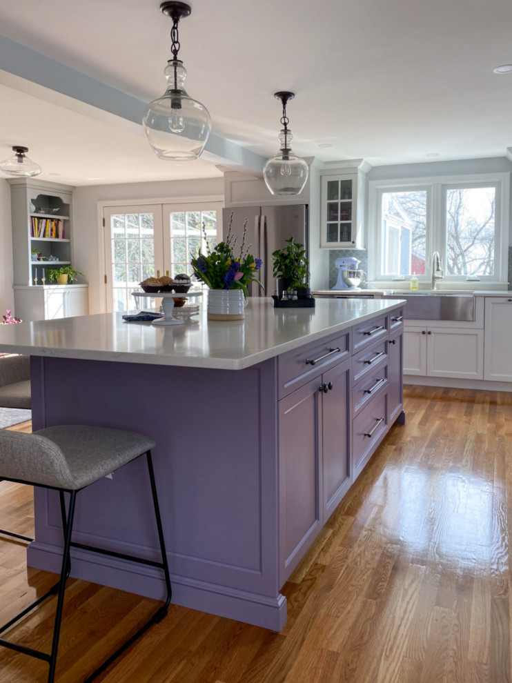 Design ideas for a transitional l-shaped kitchen in Boston with a farmhouse sink, shaker cabinets, purple cabinets, quartz benchtops, grey splashback, ceramic splashback, stainless steel appliances, light hardwood floors, with island and white benchtop.
