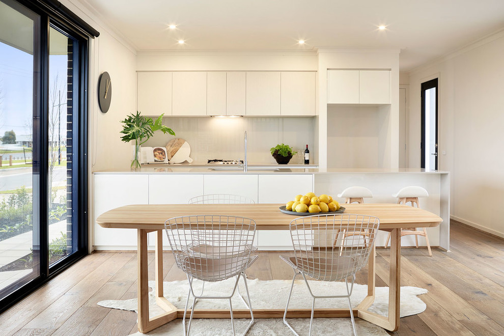 Photo of a scandinavian galley eat-in kitchen in Melbourne with an undermount sink, flat-panel cabinets, white cabinets, white splashback and light hardwood floors.