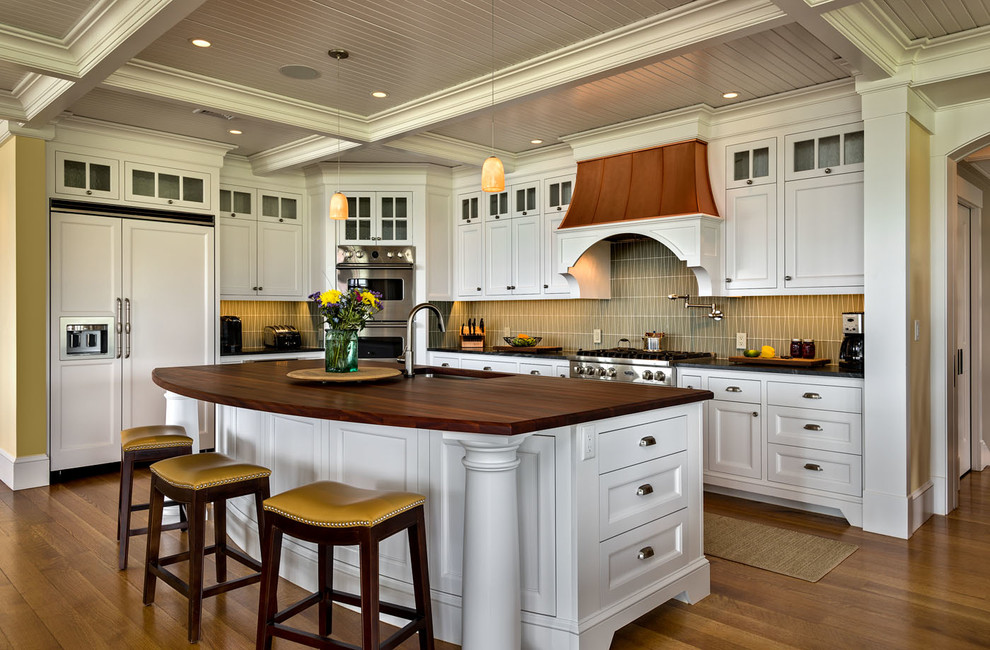 Beach style l-shaped eat-in kitchen in Boston with recessed-panel cabinets, white cabinets, wood benchtops, beige splashback, medium hardwood floors, with island, an undermount sink, subway tile splashback and stainless steel appliances.