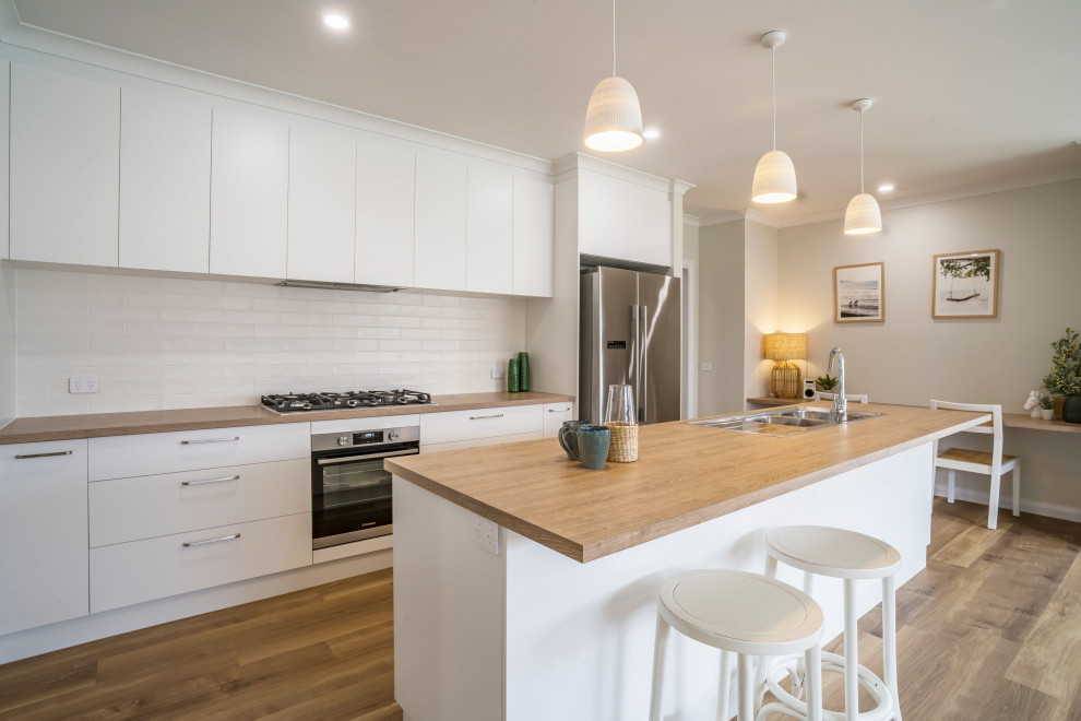 Photo of a mid-sized contemporary galley open plan kitchen in Other with a drop-in sink, flat-panel cabinets, white cabinets, laminate benchtops, white splashback, ceramic splashback, stainless steel appliances, vinyl floors, with island, green floor and brown benchtop.