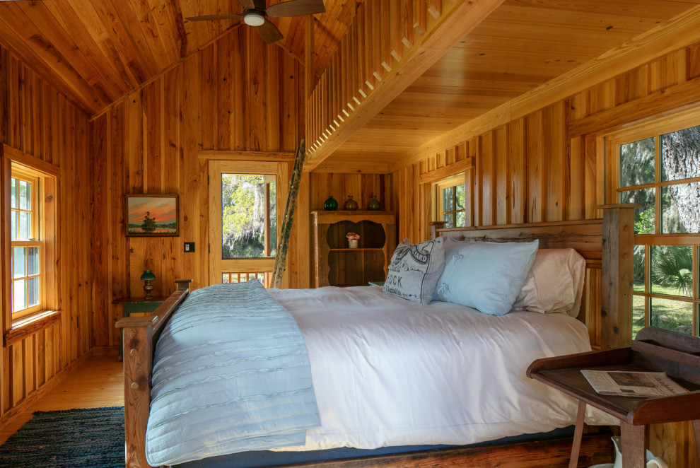 Mittelgroßes Landhausstil Hauptschlafzimmer mit hellem Holzboden, gewölbter Decke und Holzwänden in Tampa