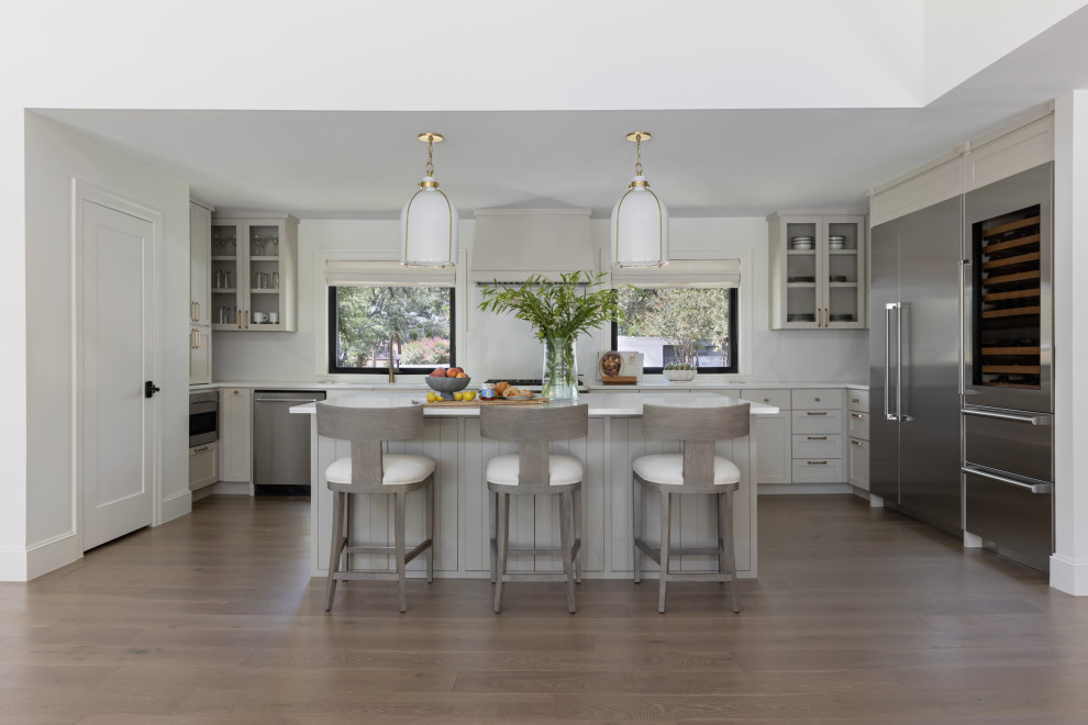 Design ideas for a transitional l-shaped open plan kitchen in Austin with shaker cabinets, grey cabinets, stainless steel appliances, dark hardwood floors, with island, brown floor and white benchtop.