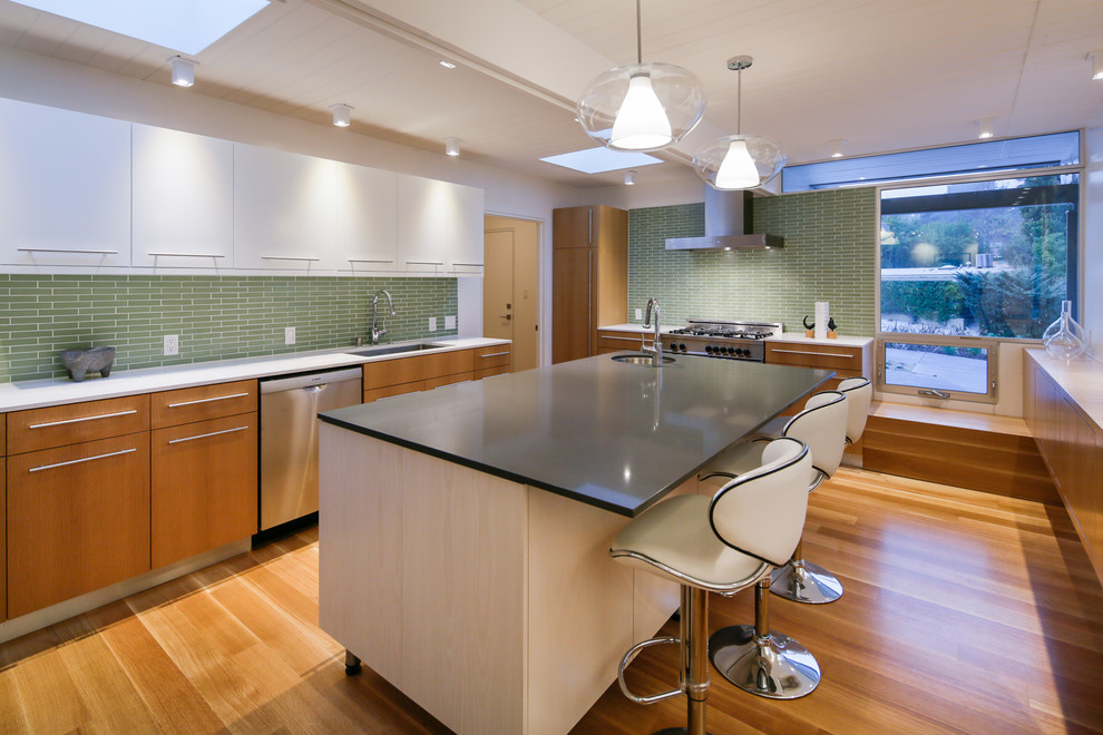 This is an example of a midcentury kitchen in Los Angeles with an undermount sink, flat-panel cabinets, white cabinets, green splashback and stainless steel appliances.