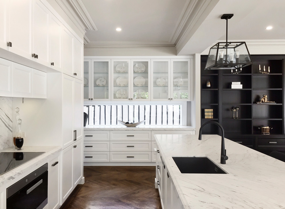 Photo of a large transitional galley open plan kitchen in Melbourne with an undermount sink, recessed-panel cabinets, white cabinets, marble benchtops, white splashback, stone slab splashback, panelled appliances, medium hardwood floors, with island and brown floor.