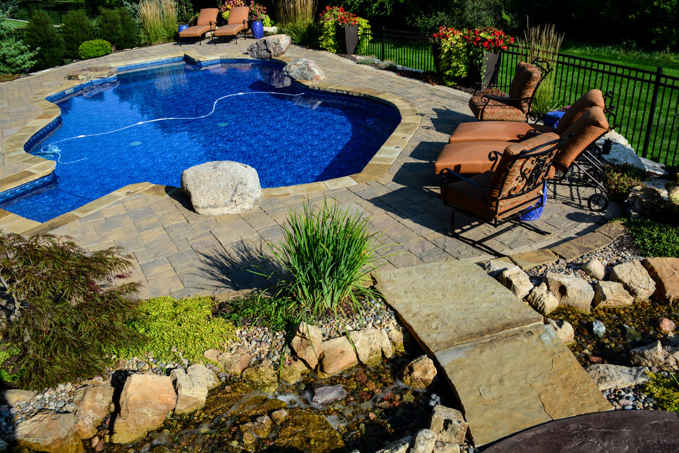 This is an example of a mid-sized country backyard custom-shaped pool in Omaha with a water feature and stamped concrete.
