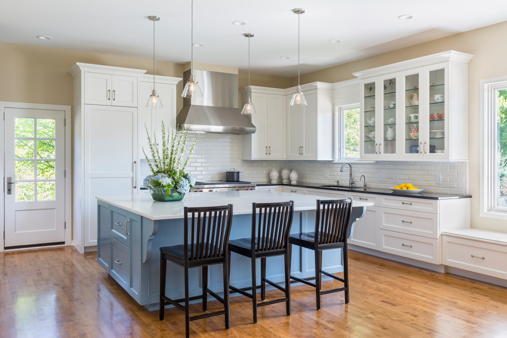 Example of a mid-sized cottage l-shaped medium tone wood floor and brown floor open concept kitchen design in Minneapolis with an undermount sink, quartz countertops, white backsplash, subway tile backsplash, stainless steel appliances, an island, black countertops, shaker cabinets and white cabinets