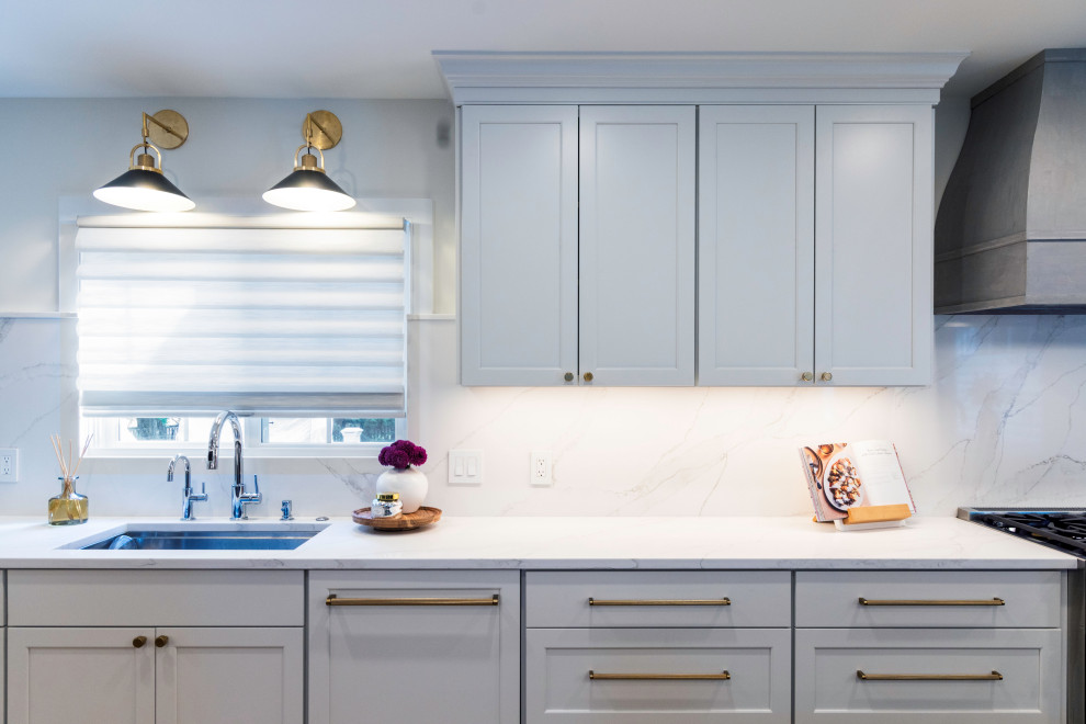 Example of a mid-sized transitional medium tone wood floor kitchen design in DC Metro with a single-bowl sink, flat-panel cabinets, quartz countertops, white backsplash, quartz backsplash, stainless steel appliances, an island and white countertops
