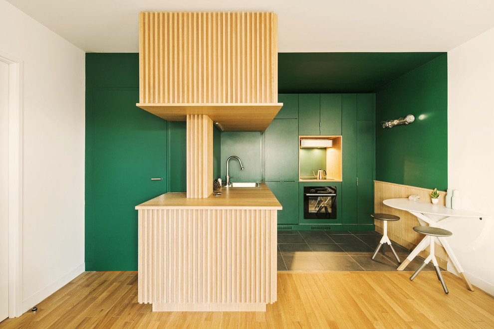 Photo of a contemporary l-shaped kitchen in Paris with a drop-in sink, flat-panel cabinets, green cabinets, wood benchtops, green splashback, black appliances, a peninsula, grey floor and beige benchtop.
