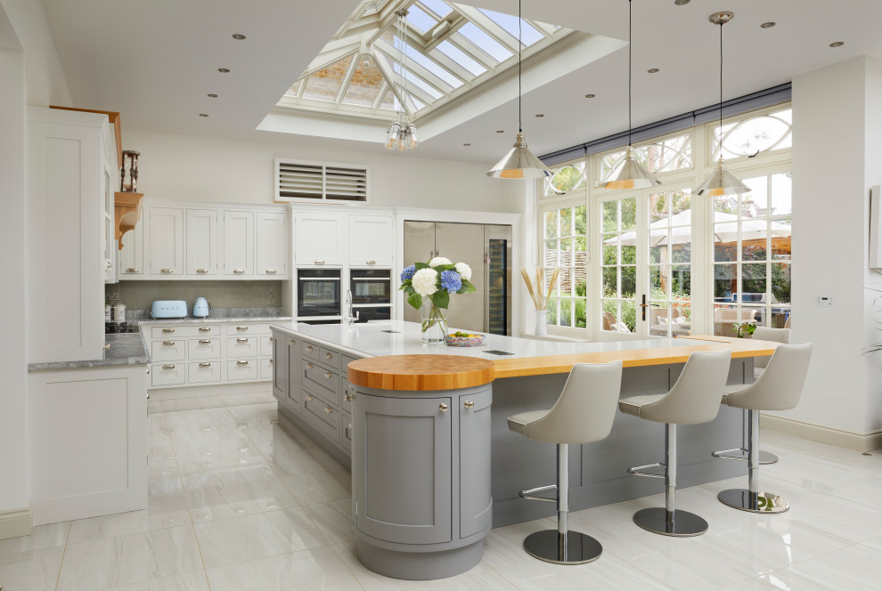 Photo of a large transitional u-shaped open plan kitchen in Essex with an undermount sink, recessed-panel cabinets, white cabinets, marble benchtops, grey splashback, marble splashback, stainless steel appliances, marble floors, a peninsula, white floor, grey benchtop and vaulted.