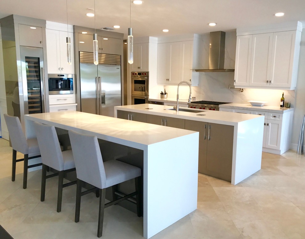 Open concept kitchen - mid-sized transitional galley travertine floor and beige floor open concept kitchen idea in Miami with an undermount sink, shaker cabinets, white cabinets, solid surface countertops, white backsplash, marble backsplash, stainless steel appliances and two islands