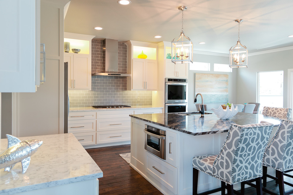 Example of a mid-sized beach style u-shaped dark wood floor eat-in kitchen design with an undermount sink, shaker cabinets, white cabinets, granite countertops, gray backsplash, glass tile backsplash, stainless steel appliances and an island