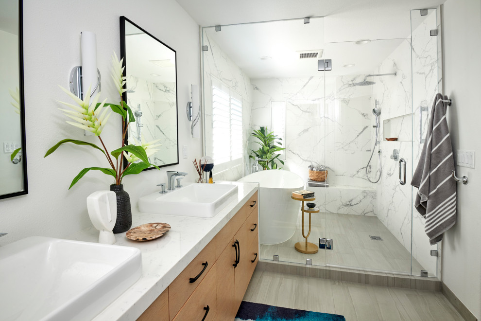 Источник вдохновения для домашнего уюта: главная ванная комната среднего размера в стиле модернизм с плоскими фасадами, светлыми деревянными фасадами, отдельно стоящей ванной, душевой комнатой, унитазом-моноблоком, белой плиткой, керамогранитной плиткой, белыми стенами, полом из керамогранита, настольной раковиной, столешницей из искусственного кварца, серым полом, душем с распашными дверями, белой столешницей, нишей, тумбой под две раковины и встроенной тумбой