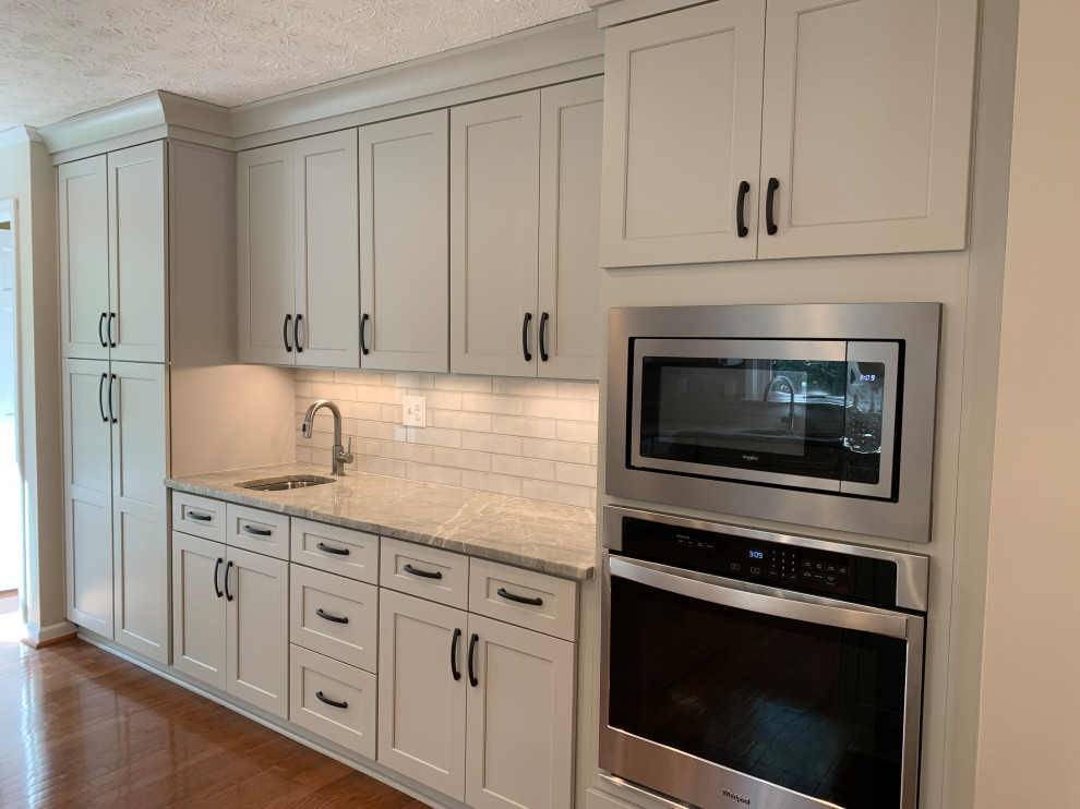 Foto på ett mellanstort vintage flerfärgad kök, med en undermonterad diskho, skåp i shakerstil, grå skåp, granitbänkskiva, grått stänkskydd, stänkskydd i tunnelbanekakel, rostfria vitvaror, mellanmörkt trägolv, en halv köksö och brunt golv
