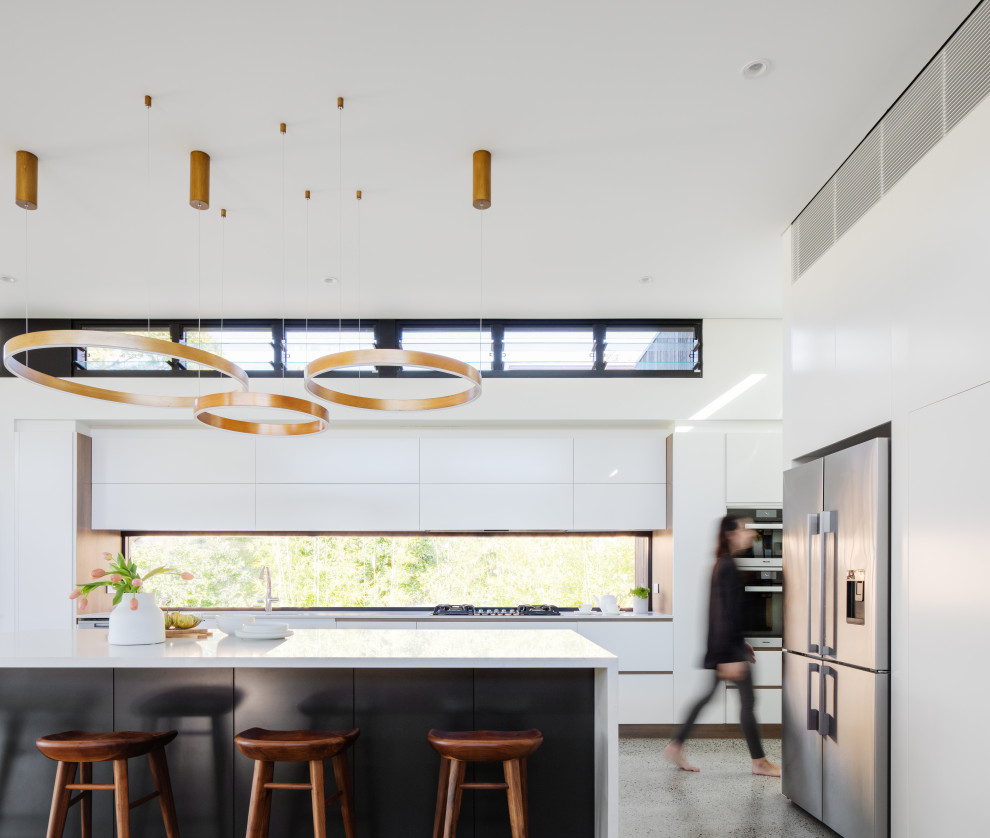 Design ideas for a contemporary l-shaped kitchen in Sydney with flat-panel cabinets, white cabinets, window splashback, stainless steel appliances, concrete floors, with island, grey floor and white benchtop.