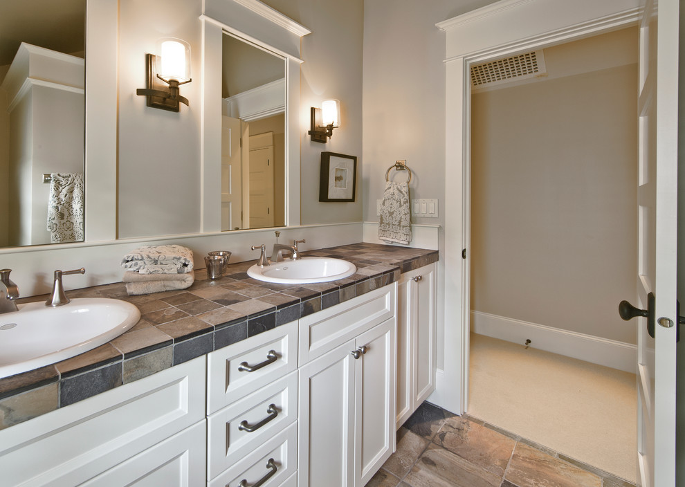 Photo of a mid-sized traditional bathroom in Seattle with a drop-in sink, recessed-panel cabinets, white cabinets, tile benchtops, beige tile, porcelain tile and grey walls.
