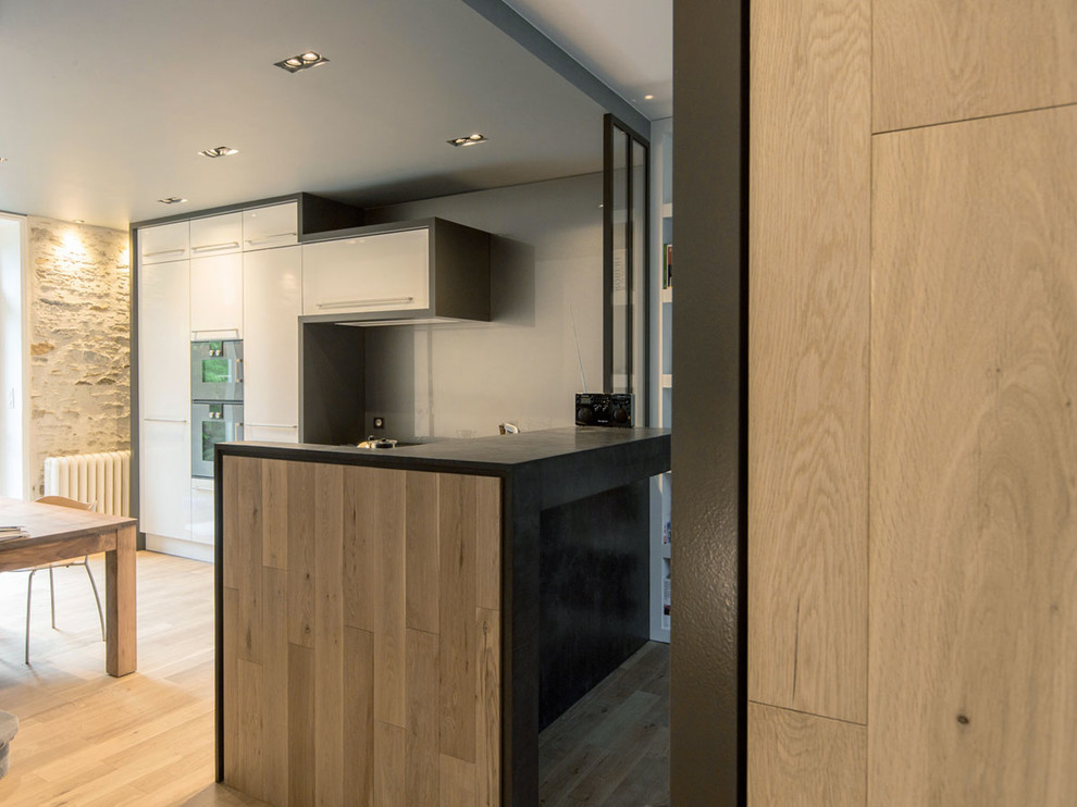 Design ideas for a mid-sized contemporary l-shaped open plan kitchen in Nantes with a double-bowl sink, beaded inset cabinets, white cabinets, concrete benchtops, grey splashback, glass sheet splashback, panelled appliances, light hardwood floors and no island.