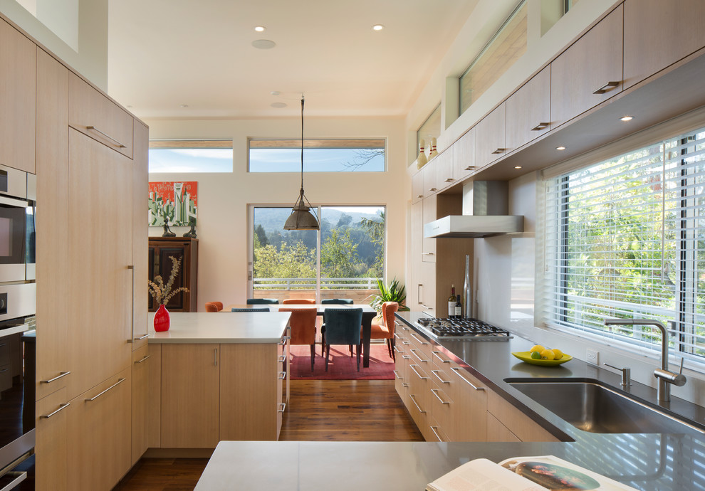 This is an example of a mid-sized contemporary u-shaped eat-in kitchen in San Francisco with an undermount sink, flat-panel cabinets, light wood cabinets, white splashback, panelled appliances, medium hardwood floors and a peninsula.