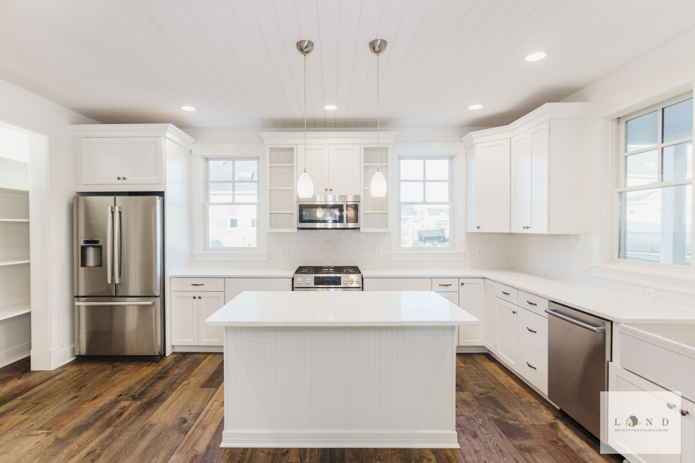 Medium sized traditional l-shaped open plan kitchen in Indianapolis with a belfast sink, white cabinets, white splashback, stainless steel appliances, dark hardwood flooring, an island, white worktops and a timber clad ceiling.