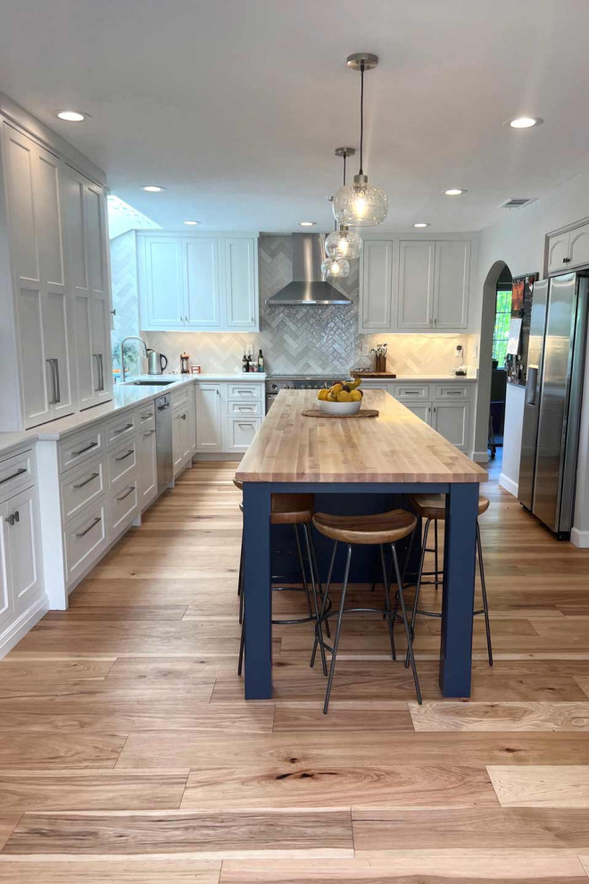Photo of a mid-sized transitional l-shaped eat-in kitchen in San Francisco with an undermount sink, shaker cabinets, white cabinets, wood benchtops, grey splashback, ceramic splashback, stainless steel appliances, light hardwood floors, with island, brown floor and brown benchtop.