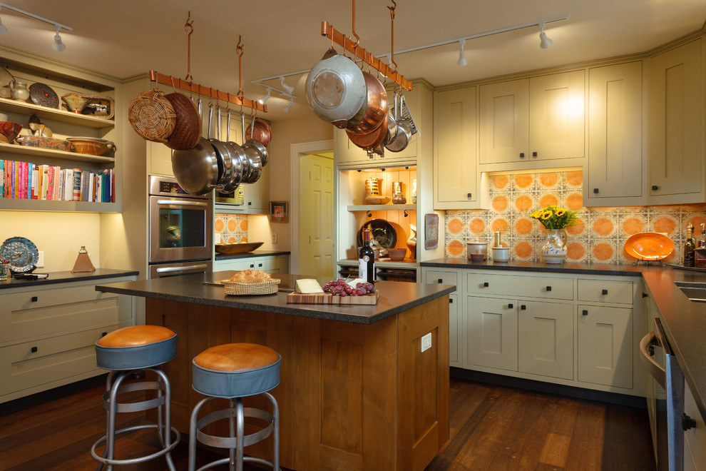 This is an example of a country u-shaped kitchen in Other with shaker cabinets, beige cabinets, orange splashback, mosaic tile splashback, stainless steel appliances, medium hardwood floors, with island and brown floor.