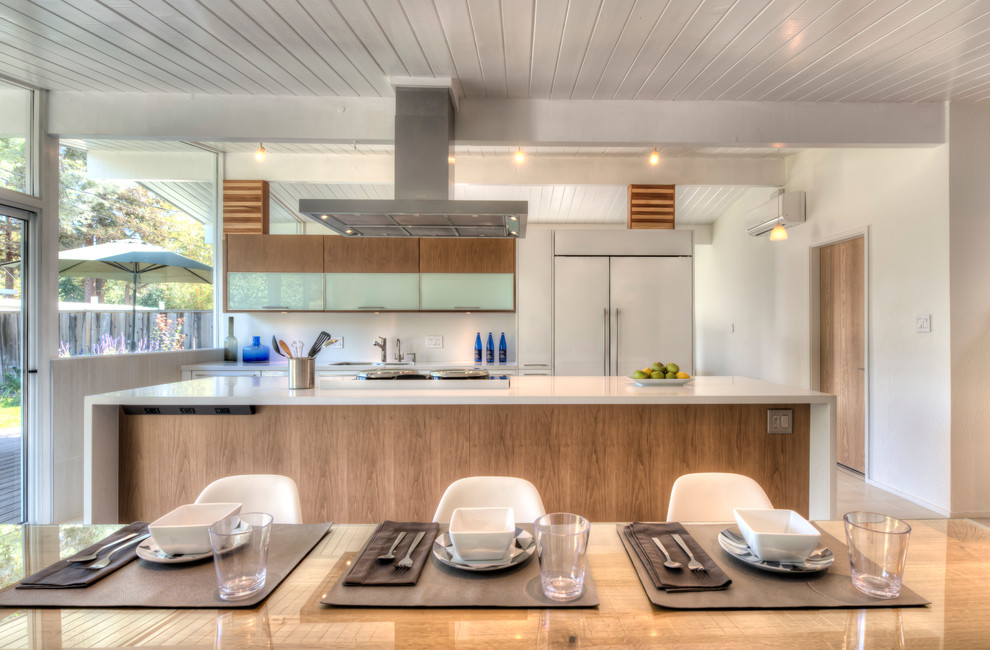 Inspiration for a mid-sized transitional single-wall porcelain tile eat-in kitchen remodel in Nice with a single-bowl sink, flat-panel cabinets, white cabinets, solid surface countertops, white backsplash, porcelain backsplash, paneled appliances and an island