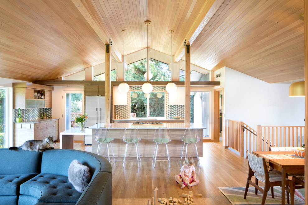 This is an example of a mid-sized midcentury l-shaped open plan kitchen in Seattle with medium hardwood floors, brown floor, an undermount sink, flat-panel cabinets, light wood cabinets, multi-coloured splashback, stainless steel appliances, with island and white benchtop.