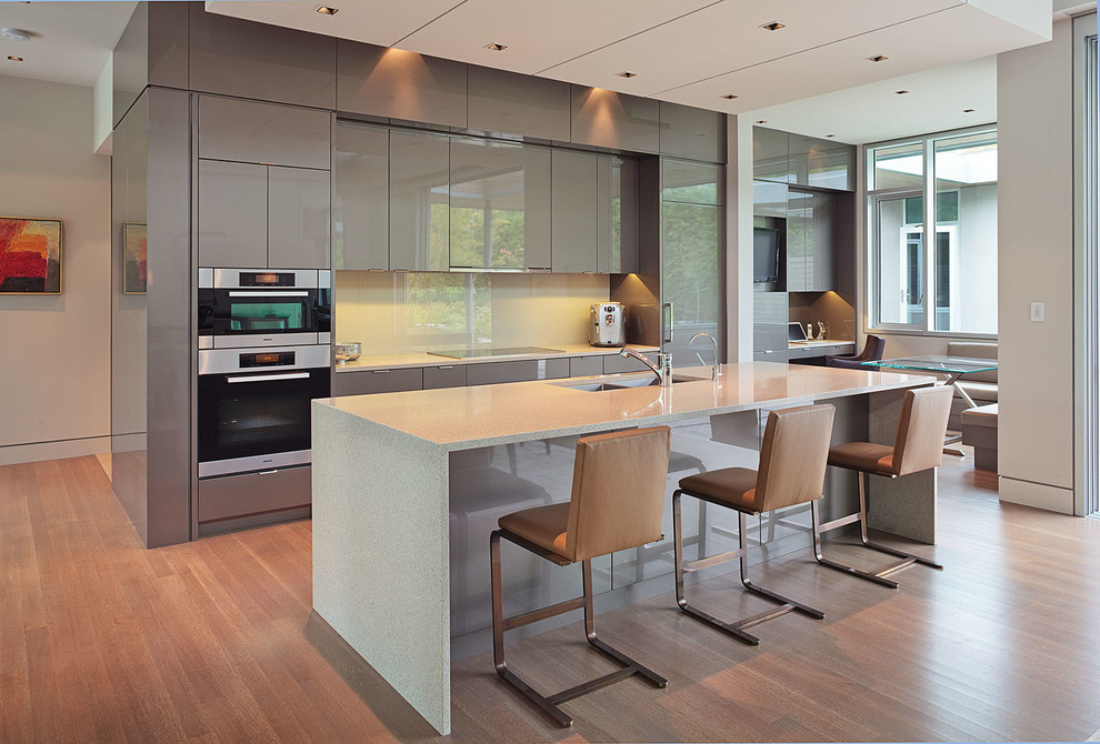 This is an example of a contemporary galley kitchen in Vancouver with an undermount sink, flat-panel cabinets, grey cabinets, white splashback, glass sheet splashback and panelled appliances.