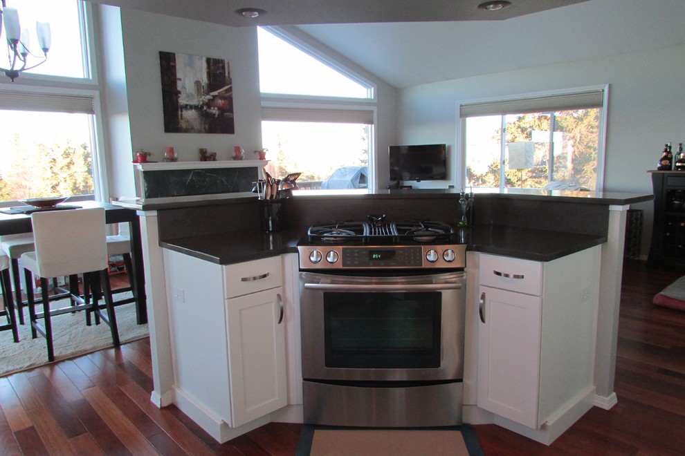 Mid-sized transitional l-shaped medium tone wood floor eat-in kitchen photo with a double-bowl sink, recessed-panel cabinets, white cabinets, gray backsplash, stainless steel appliances, an island, quartz countertops and glass tile backsplash