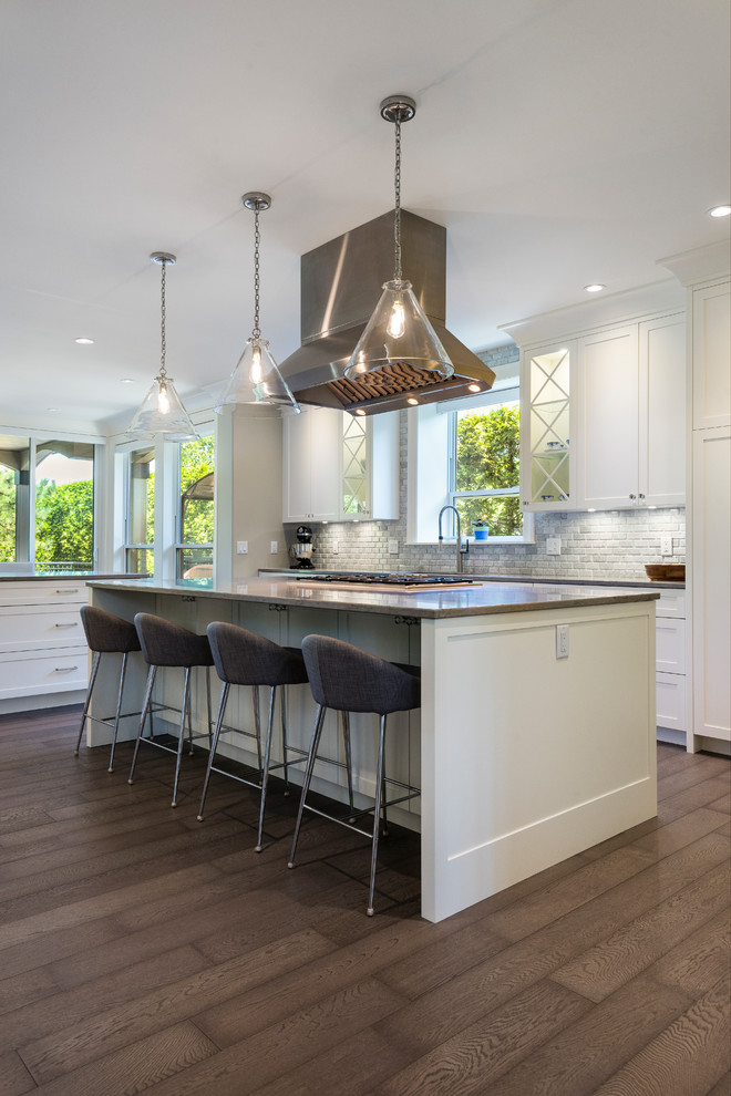 Photo of a large traditional u-shaped open plan kitchen in Vancouver with an undermount sink, shaker cabinets, white cabinets, quartz benchtops, white splashback, stone tile splashback, stainless steel appliances, medium hardwood floors, multiple islands and brown floor.