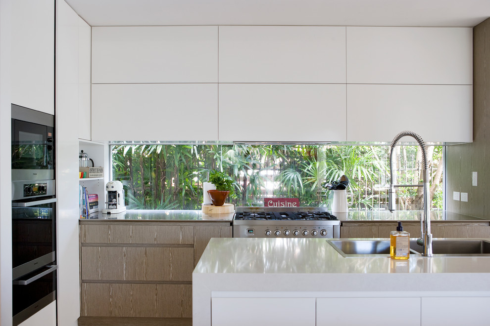 This is an example of a mid-sized contemporary galley kitchen in Sydney with a double-bowl sink, flat-panel cabinets, white cabinets, stainless steel appliances and with island.