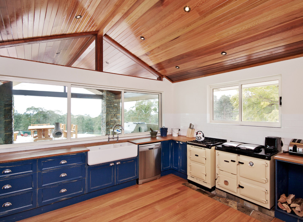 Photo of a large country u-shaped eat-in kitchen in Other with a farmhouse sink, beaded inset cabinets, blue cabinets, wood benchtops, white splashback, subway tile splashback, coloured appliances, light hardwood floors and a peninsula.