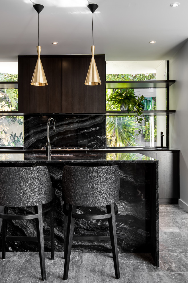 Photo of a mid-sized modern galley eat-in kitchen in Perth with a single-bowl sink, dark wood cabinets, marble benchtops, black splashback, stone slab splashback, black appliances, ceramic floors, with island and flat-panel cabinets.