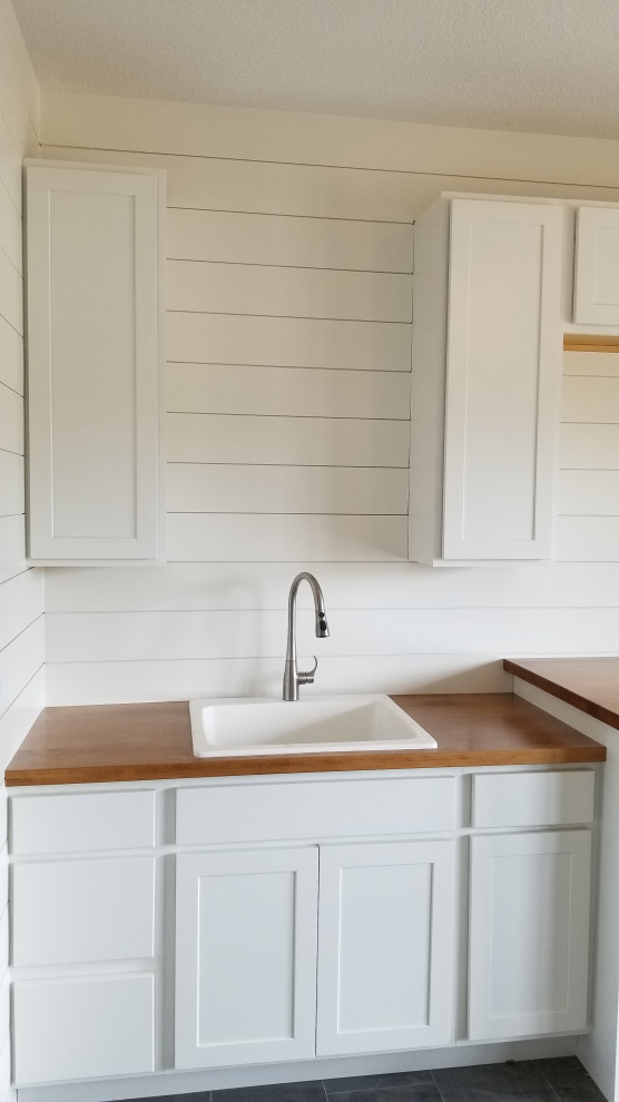 This is an example of a mid-sized modern single-wall dedicated laundry room in Other with a drop-in sink, recessed-panel cabinets, white cabinets, wood benchtops, white splashback, shiplap splashback, white walls, ceramic floors, a side-by-side washer and dryer, grey floor, brown benchtop and planked wall panelling.