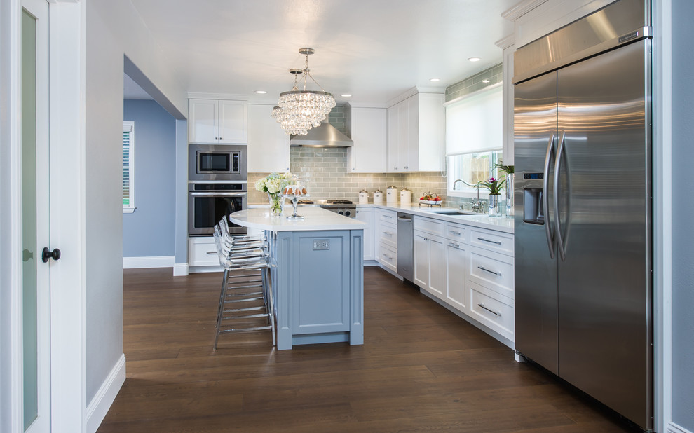 Mid-sized transitional l-shaped eat-in kitchen in Los Angeles with a double-bowl sink, recessed-panel cabinets, white cabinets, quartz benchtops, grey splashback, ceramic splashback, stainless steel appliances, medium hardwood floors and with island.