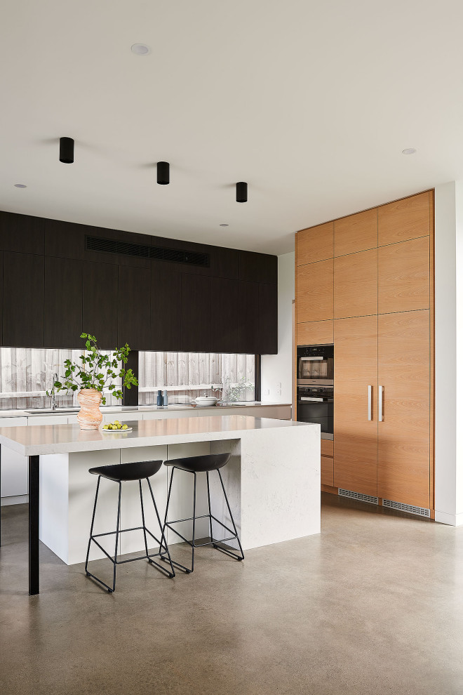 Inspiration for a mid-sized contemporary galley open plan kitchen in Geelong with an undermount sink, flat-panel cabinets, quartzite benchtops, glass sheet splashback, black appliances, concrete floors, with island, grey floor and white benchtop.