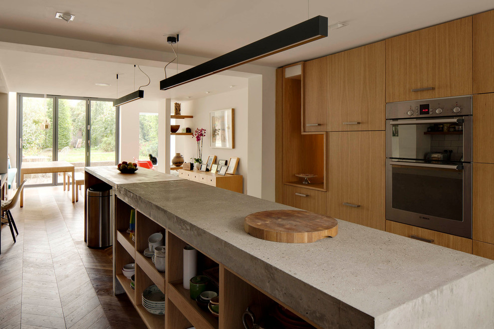Design ideas for a mid-sized galley eat-in kitchen in London with an undermount sink, flat-panel cabinets, light wood cabinets, concrete benchtops, grey splashback, stone slab splashback, stainless steel appliances, medium hardwood floors and with island.