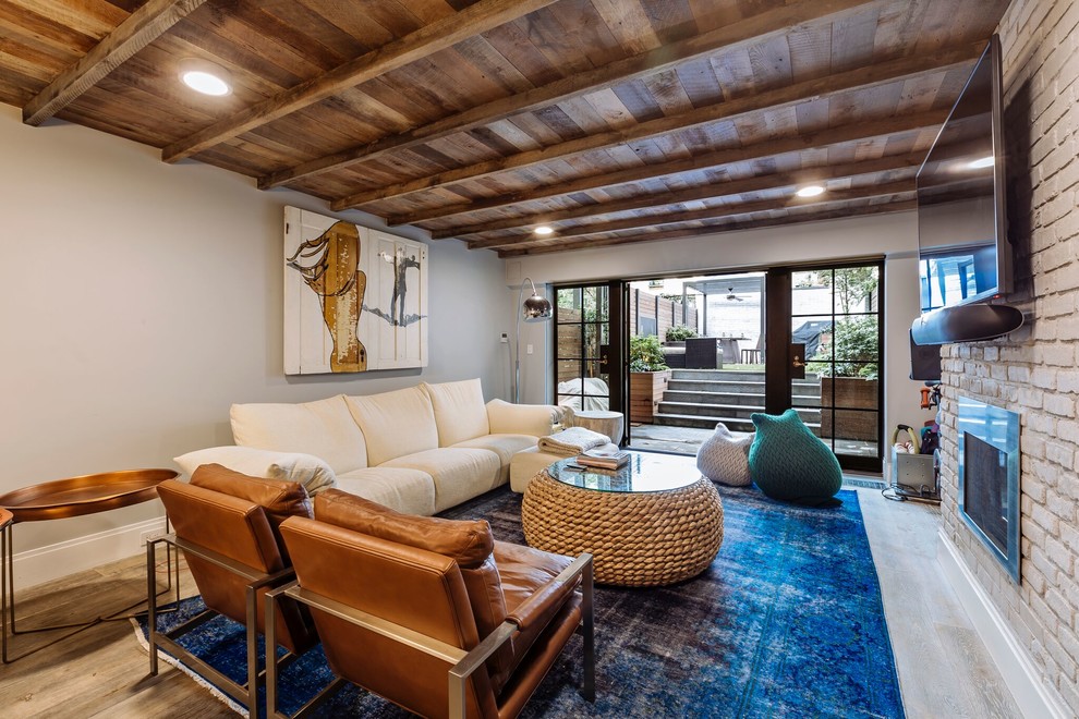 Large contemporary open concept family room in New York with light hardwood floors, white walls, a brick fireplace surround, a wall-mounted tv, beige floor, a two-sided fireplace, exposed beam and brick walls.
